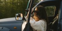 A woman using binoculars to observe nature from her car during a sunny day.